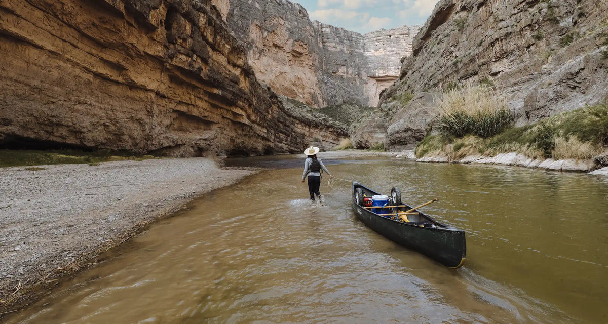 A person pulling a canoe down a river in a large canyon.