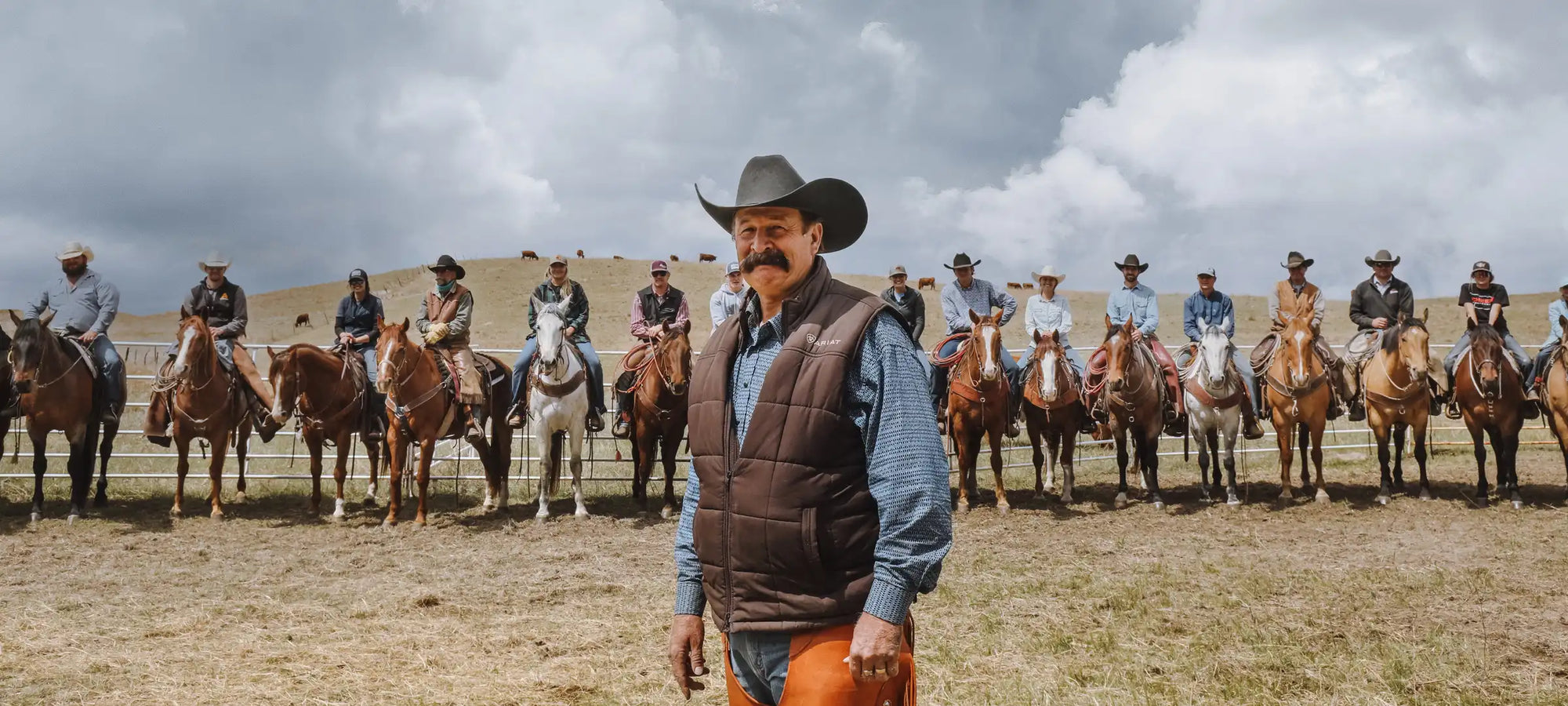 A real life cowboy standing in front of a line of cowboys on their horses.