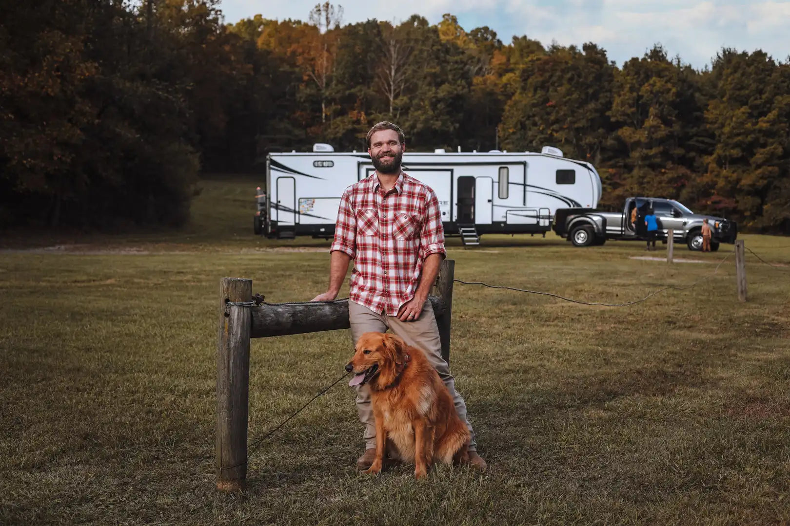 A man with his dog standing with his truck and fifth wheel rv in the background.