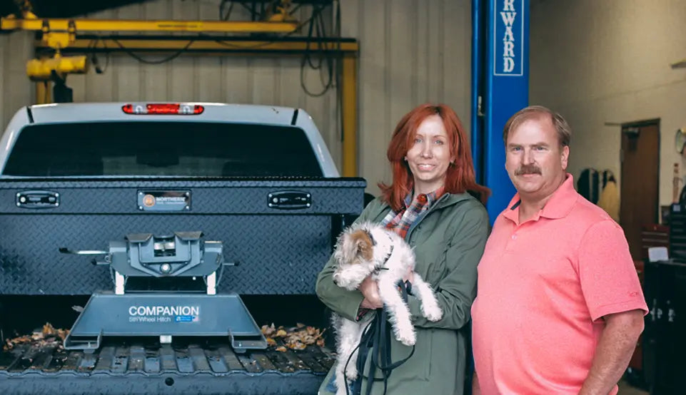 A couple holding their dog standing in front of a pickup bed with a B&W fifth wheel hitch.