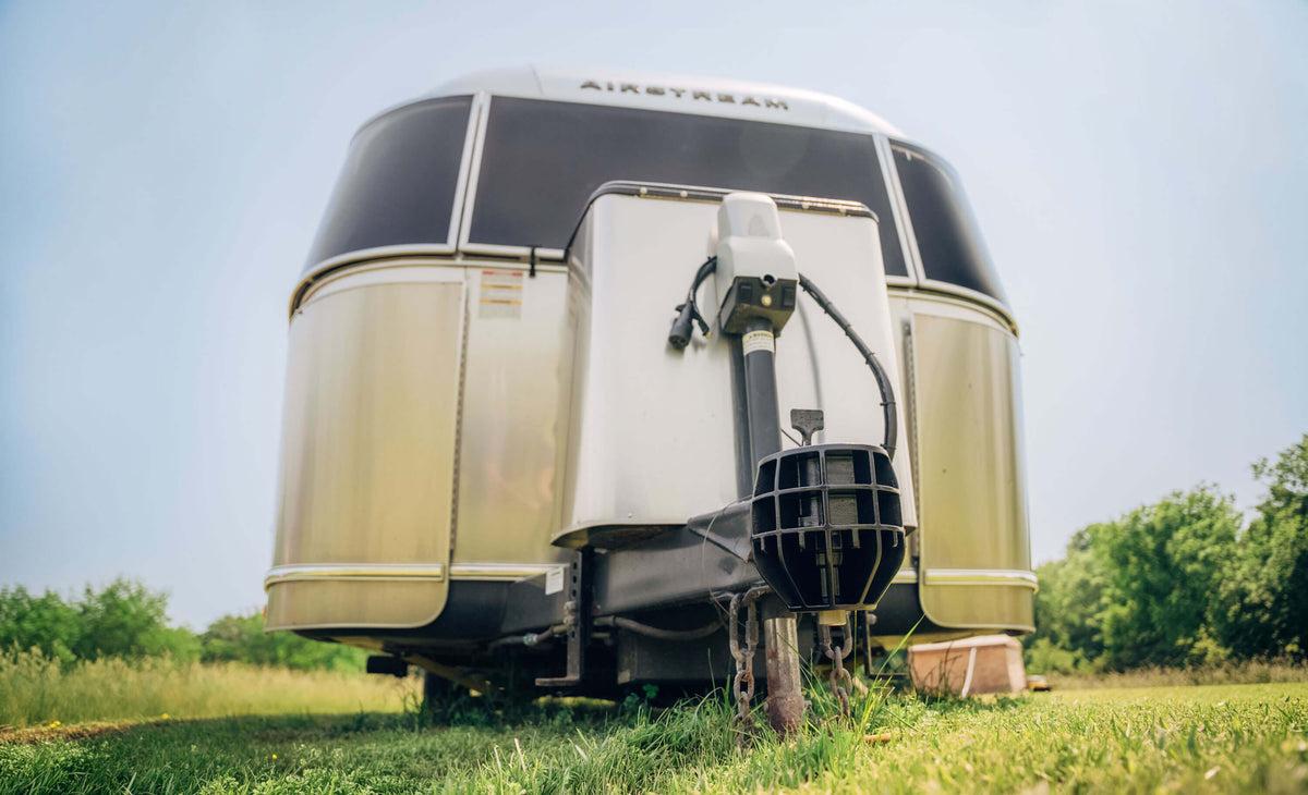 An Airstream travel trailer sitting on green grass with a blue sky with a black icon bumper-pull coupler lock attached.