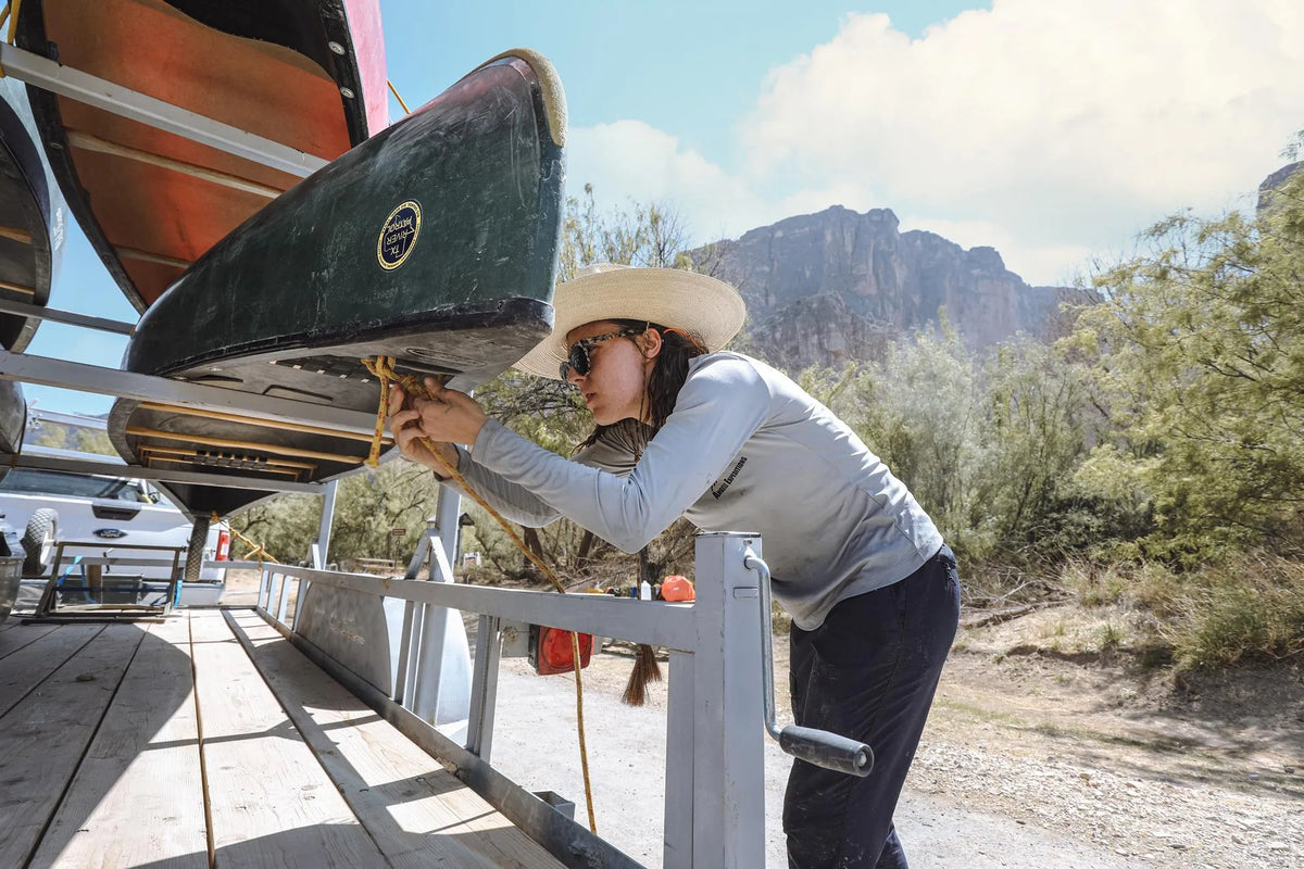 A woman securing a canoe on a vehicle with mountains in the background