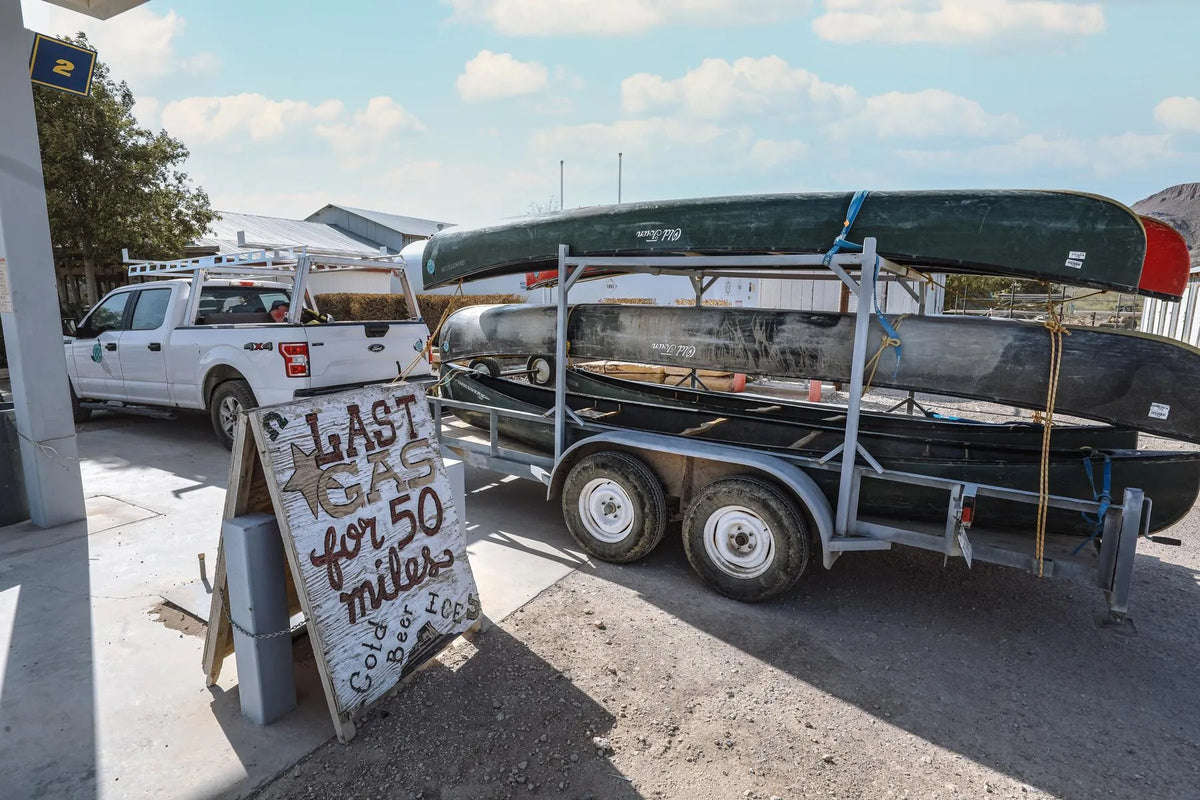 Trailer with canoes at a gas station with a sign advertising gas, cold beer, and ice.