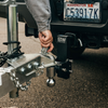 Close-up of a hand connecting a tow & stow adjustable trailer hitch to a shiny trailer coupler, and there's a Washington license plate visible on the back of the pickup.