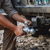 A man outdoors at the rear of a vehicle, attaching a tow & stow ball hitch mount to  the receiver of a pickup truck