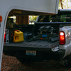 A white pickup truck parked outdoors with its tailgate open, showing the back of the truck bed loaded with gear, including a B&W Companion Fifth Wheel Slider hitch.
