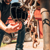 A close-up shot of a man locking a B&W Icon bumper-pull coupler lock with farm equipment and a barn in the background.