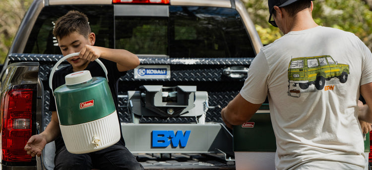 a man and his son are holding coolers in the bed of a pickup truck with a B&W companion fifth wheel hitch installed in the back.