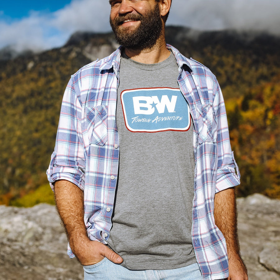 a man wearing a b&w towing adventure tshirt under his flannel shirt that is unbuttoned 