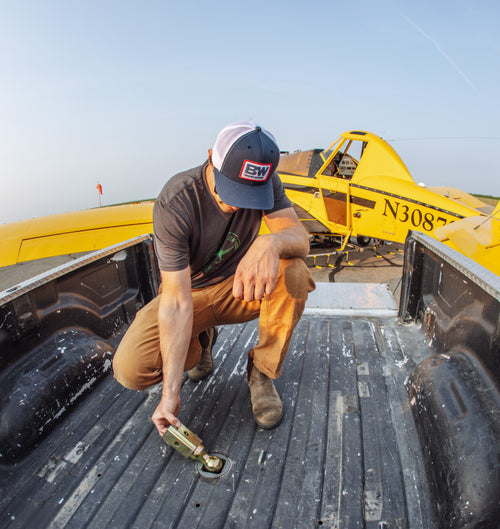 a man flipping over a turnoverball gooseneck ball to store it in his pickup bed and there's a yellow crop duster plane in the background