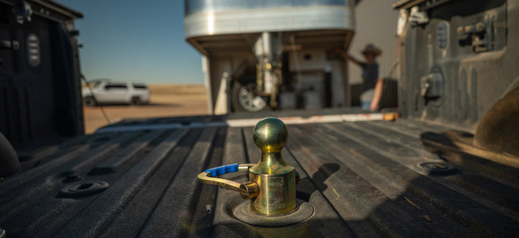 a B&W oem gooseneck ball installed in the back of a pickup truck bed with a gooseneck trailer close behind the truck.