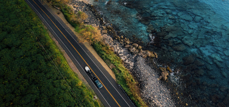 a high drone shot of a pickup hauling a wave runner down with a Tow & Stow hitch along a seaside rode.