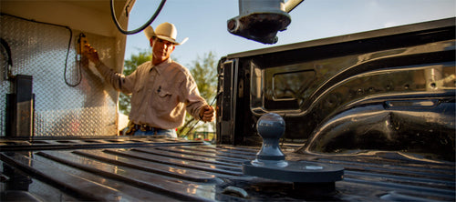 Man in a cowboy hat hooking up a gooseneck trailer with a B&W Turnoverball Gooseneck Hitch in the pickup bed.