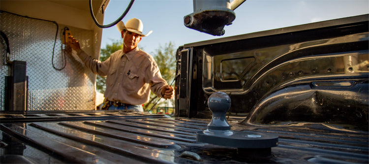 Man in a cowboy hat hooking up a gooseneck trailer with a B&W Turnoverball Gooseneck Hitch in the pickup bed.