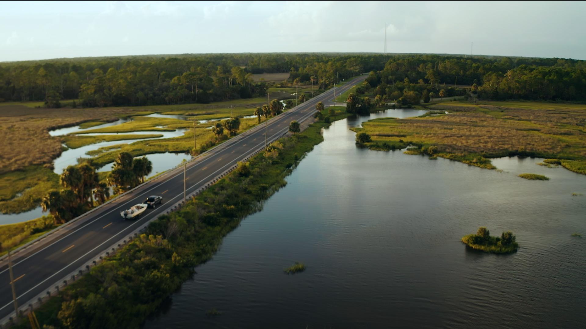 A truck towing a boat along a road between Florida salt marshes. 